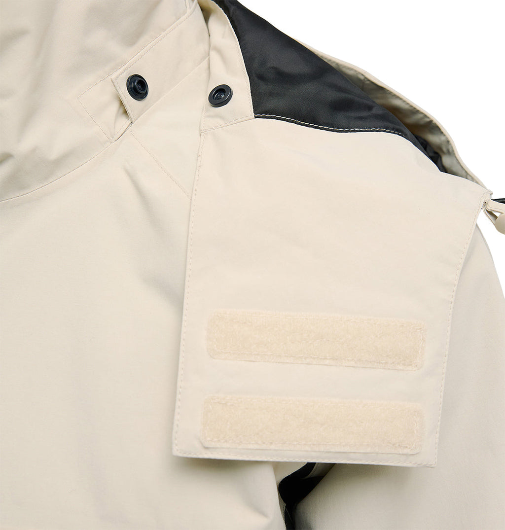A close-up of the Mountain Lab Jacket 20K by DC Shoes in light beige, showcasing a shoulder epaulet with two horizontal Velcro strips and black buttons. Engineered for optimal snow performance, this jacket features a black accent on the upper shoulder and delivers breathable protection during challenging weather conditions.