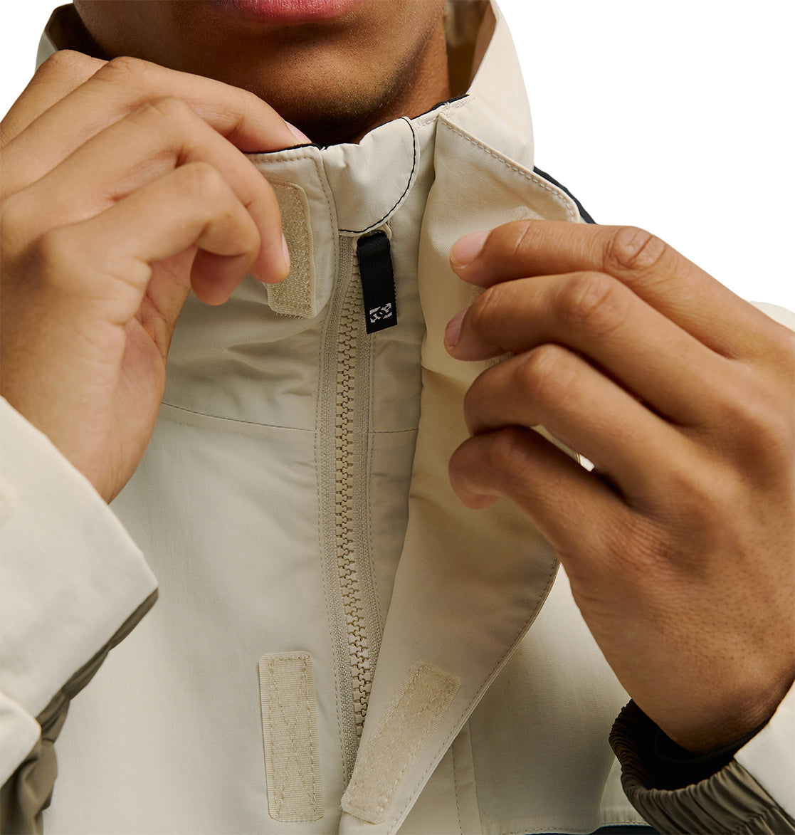 A person zipping up the DC Shoes Mountain Lab Jacket 20K, with their hands holding the collar and zipper. The image focuses on the hands and upper torso, with the person’s face partially visible, highlighting the breathable protection offered by this high-performance jacket.