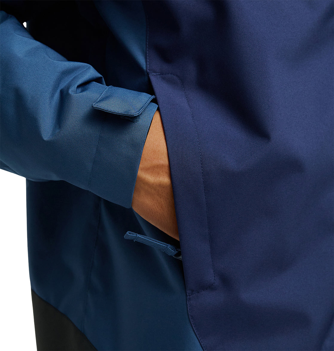 A person’s hand is partially inside the side pocket of the DC Shoes Coldsmoke Jacket 10K, a dark blue jacket engineered for exceptional snow performance. The image highlights the pocket and sleeve details, emphasizing its stylish construction and integrated waterproofing.