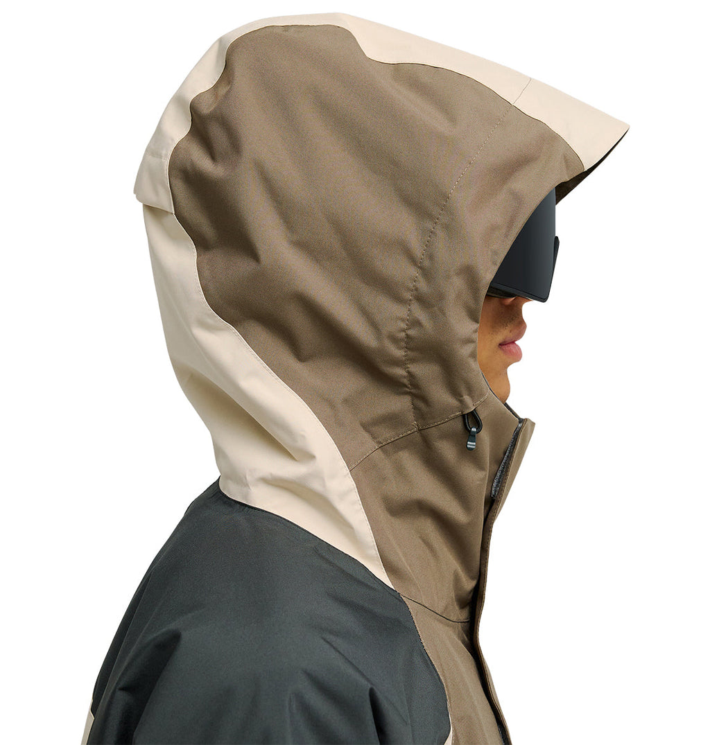 A person in profile wears the DC Shoes Coldsmoke Jacket 10K— a tan and beige hooded jacket designed for breathable protection—paired with large black goggles, set against a white background.