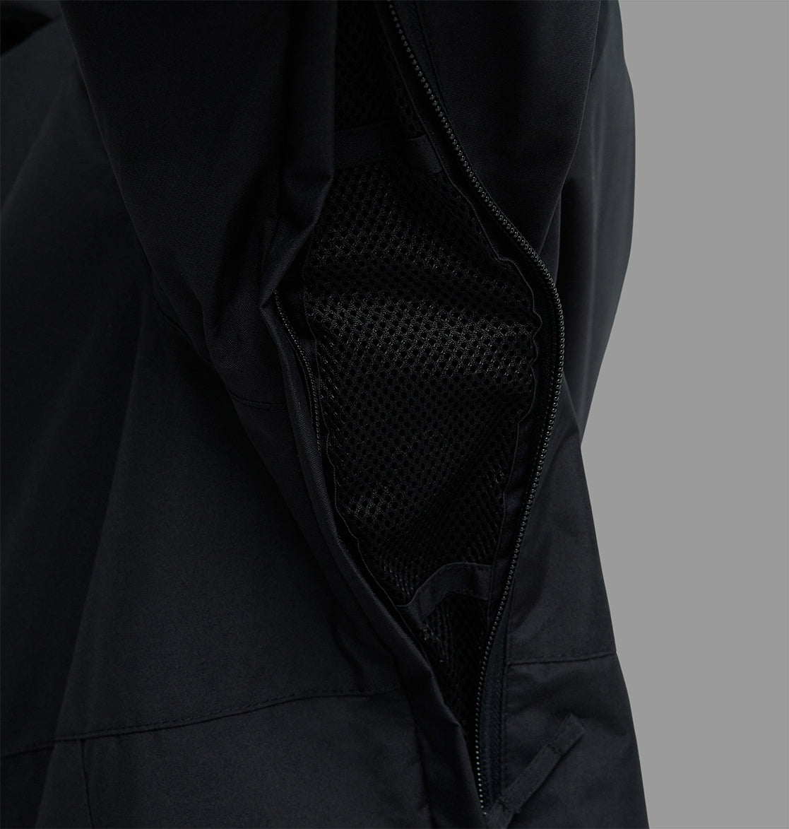 Close-up of the DC Shoes Basis Jacket 10K in black, featuring an open zipper vent with black mesh lining underneath, set against a plain gray background.