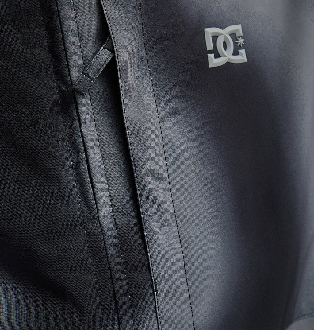 Close-up of the DC Shoes Basis Jacket 10K, a black insulated ski jacket featuring a front pocket with a flap and the white DC Shoes logo printed on the chest.