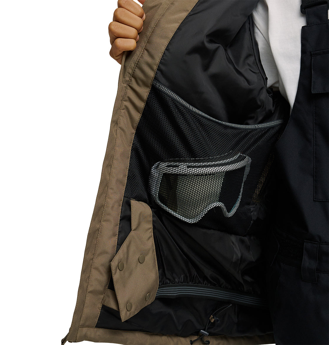 A person holds open the DC Shoes Basis Jacket 10K, revealing its mesh inner pocket containing a pair of ski or snowboard goggles.