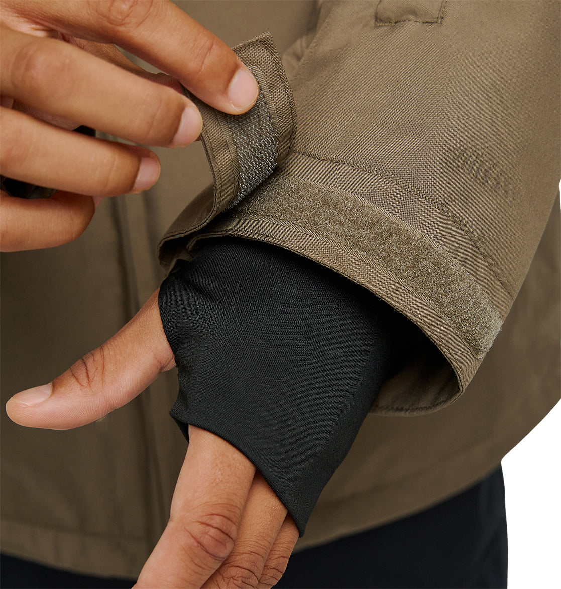 A person adjusts the Velcro cuff of a brown DC Shoes Basis Jacket 10K sleeve, revealing a black inner sleeve with a thumb hole over their hand. This insulated, breathable jacket from DC Shoes ensures comfort and protection, making it ideal for challenging conditions.