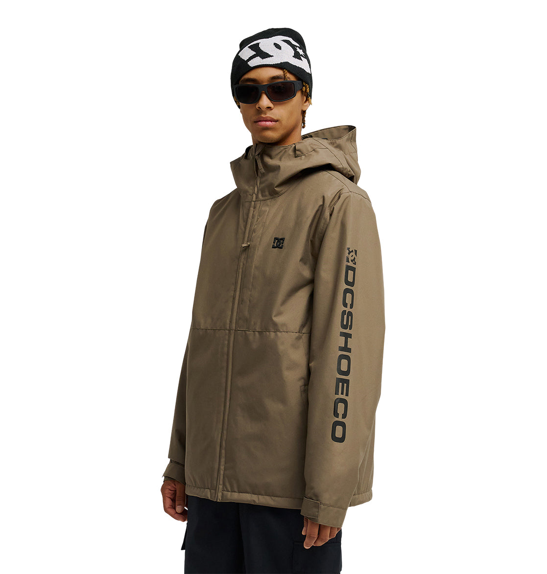 A person wearing the DC Shoes Basis Jacket 10K in tan with “DCSHOECO” on the sleeve, paired with a black beanie featuring a white design and sunglasses, standing against a plain white background.