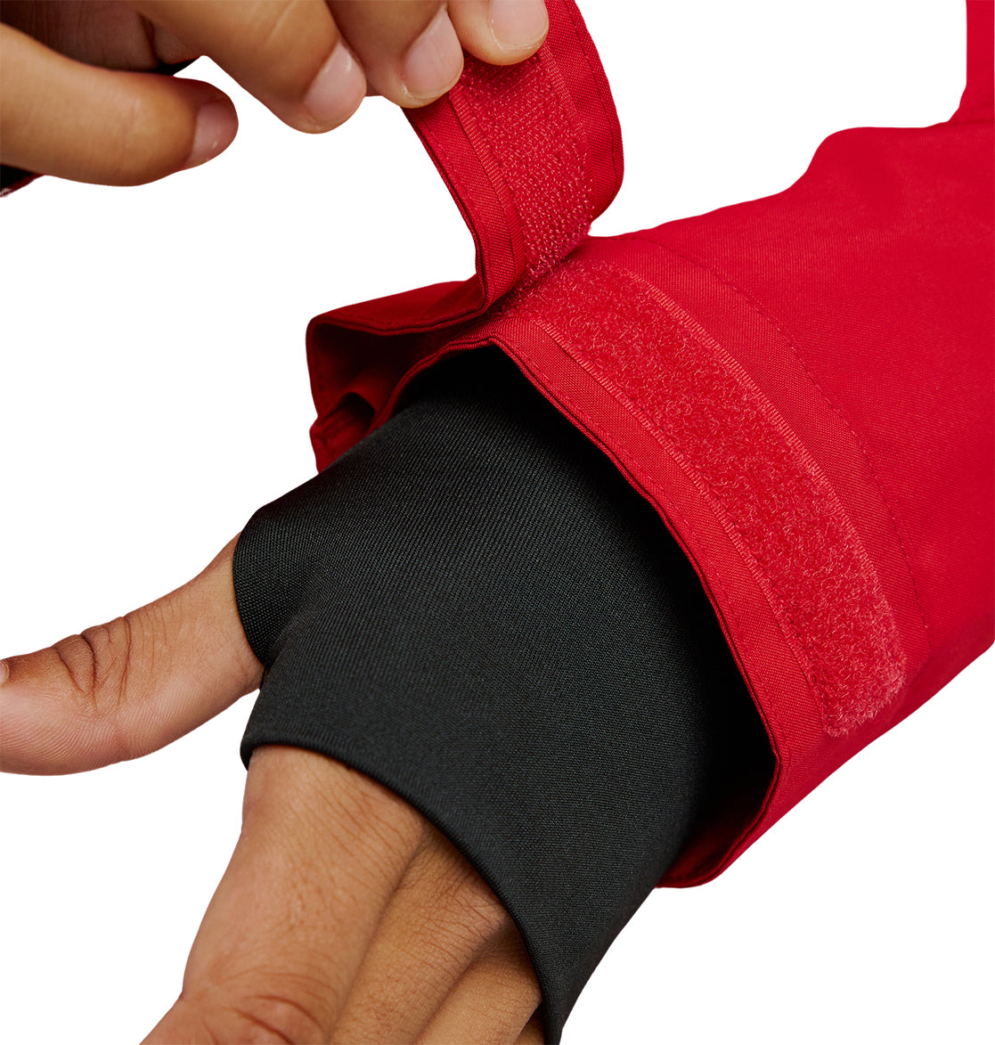 A person adjusts the Velcro cuff of the red DC Shoes Basis Jacket 10K, revealing a black inner sleeve covering part of their hand, against a white background.