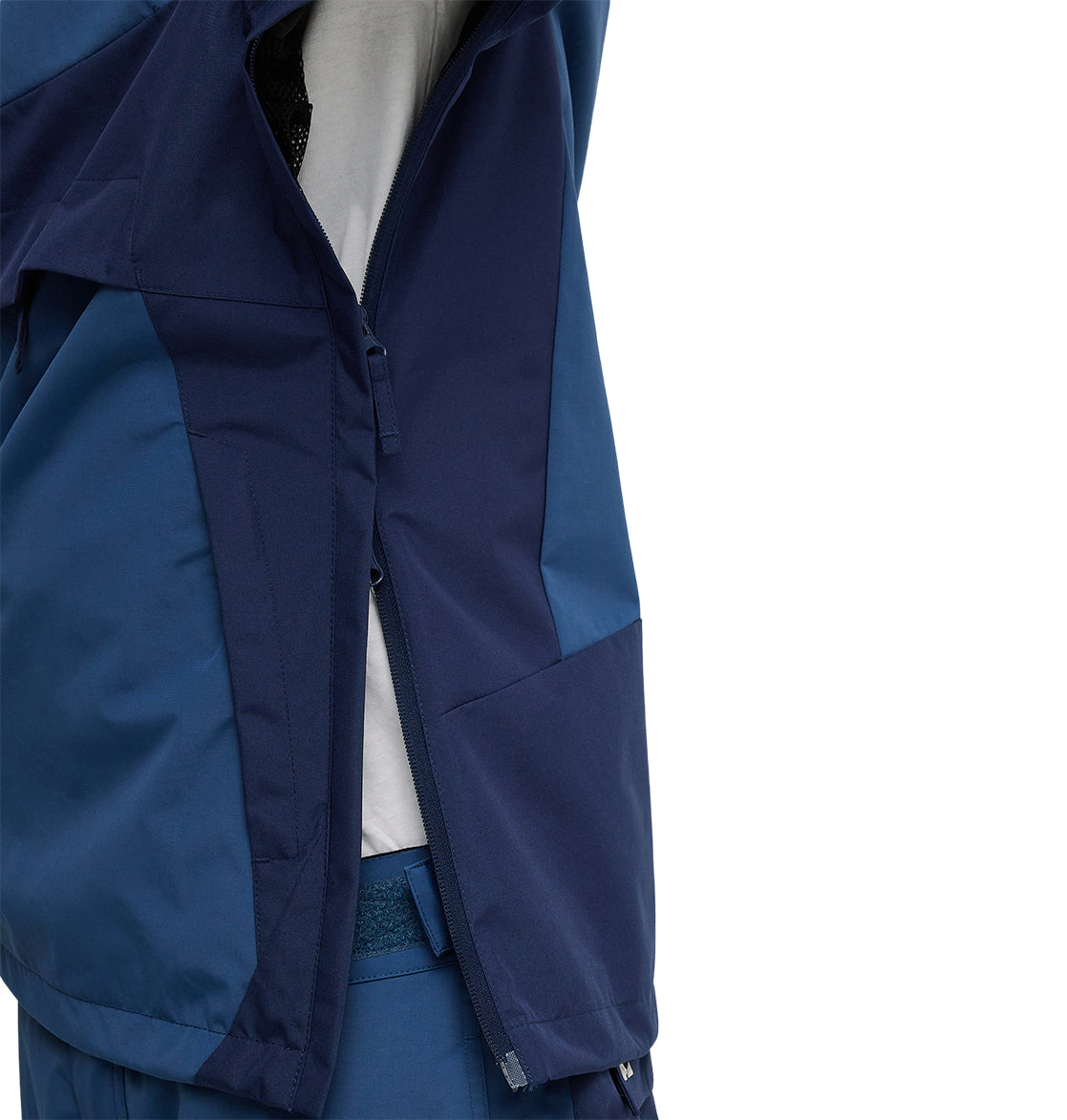 Wearing the DC Shoes Mountain Lab Anorak 10K in blue and navy, a person unzips the side vent of the jacket, revealing a white shirt underneath—showcasing the Mountain Lab Anorak 10K’s breathable protection engineered for top snow performance.