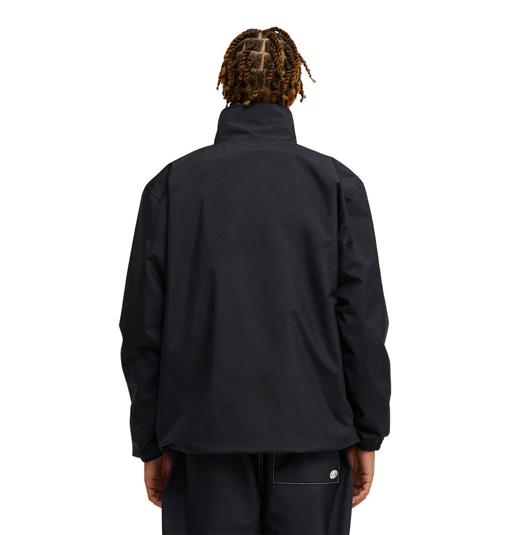 A person with short, twisted hair is shown from behind, wearing the DC Shoes Park Reversible Anorak and black pants against a plain white background. The jacket has a high collar, loose fit, and provides dependable waterproofing for excellent snow performance. Their hands rest relaxed at their sides.