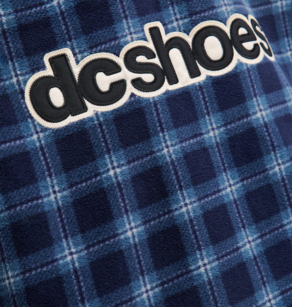 Close-up of blue plaid fabric on the Park Reversible Anorak by DC Shoes, featuring the brand’s logo embroidered in bold black and white letters across the material, highlighting its snow performance qualities.