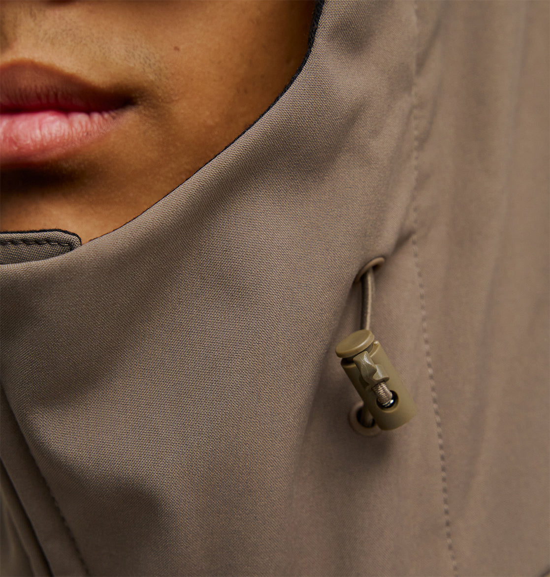 Close-up of a person’s lower face and neck, wearing the DC Shoes Spectrum Softshell Jacket in taupe, featuring a visible drawstring and plastic cord lock.
