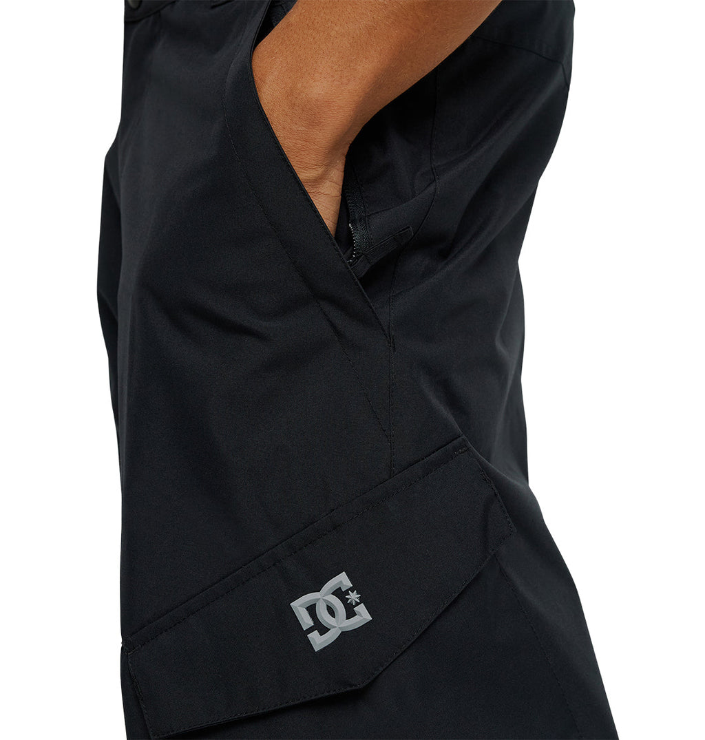 A person wearing black DC Shoes Banshee Pants with one hand in a pocket. The DC Shoes logo is visible near the knee.