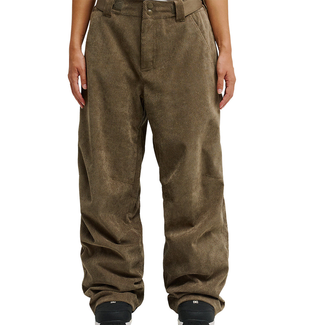 A person is wearing DC Shoes’ Snow Carpenter Pant 10K in loose-fitting brown corduroy, paired with black shoes. Shown from waist to feet against a white background, their hands rest at their sides. The pants feature a textured, ribbed design that delivers comfort and weather protection.