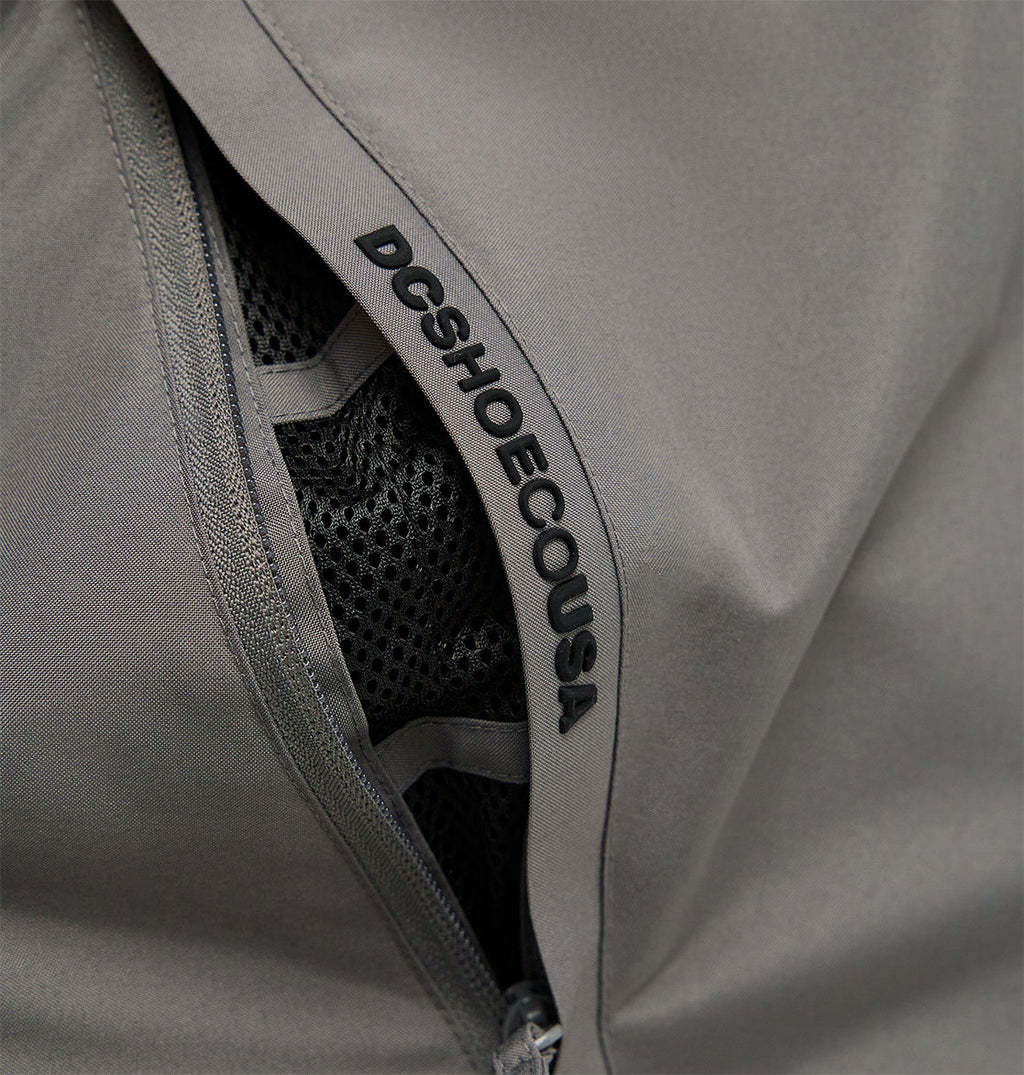 Close-up of a gray zippered pocket on the Smoke Pants 10K by DC Shoes, featuring black mesh lining for breathable comfort and “DCSHOECOUSA” printed along the zipper seam.