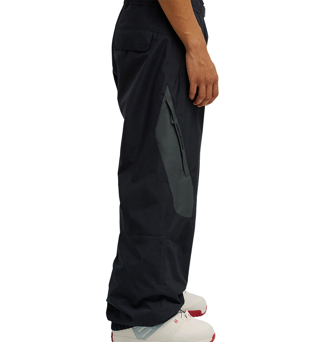 A person wearing DC Shoes Smoke Pants 10K—black pants with a gray zipper pocket—paired with white sneakers, shown from the side against a white background. The Smoke Pants 10K provide breathable protection for all-day comfort.