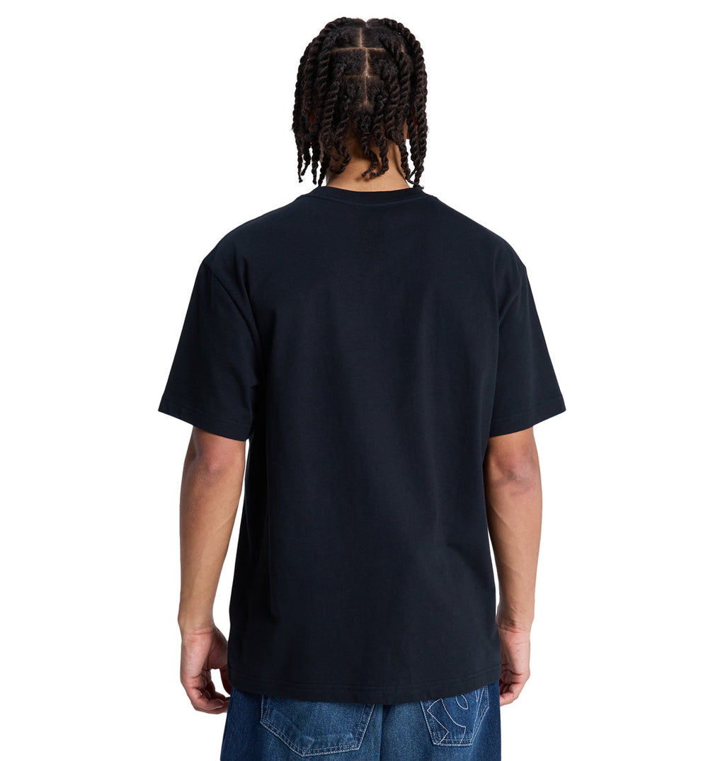 A person with braided hair stands with their back to the camera, wearing a plain black Reebok DC Star Filled Hss T-shirt and blue jeans against a white background.