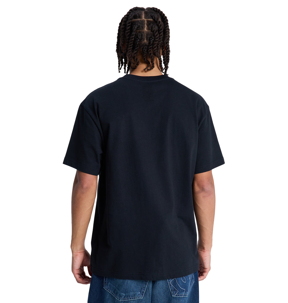 A person with braided hair stands with their back to the camera, wearing a plain black Reebok DC Star Filled Hss T-shirt and blue jeans against a white background.
