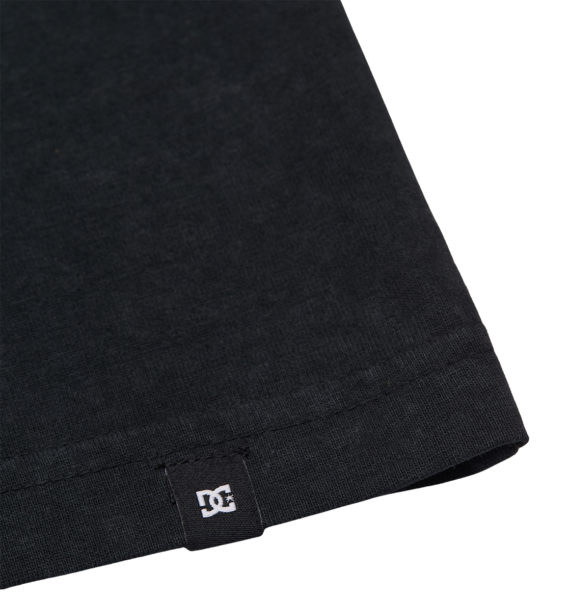 Close-up of the bottom hem of the Men's DC Star Struck Tee by DC Shoes, featuring a small black fabric tag with the white DC Shoes logo sewn into the hem.