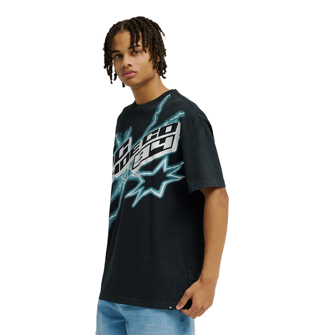 A man is seen wearing the Men's DC Star Struck Tee from DC Shoes—a black graphic skate T-shirt featuring bold blue lightning and starburst designs—while facing slightly to the side against a plain white background. The relaxed fit tee is styled with light blue jeans for an effortlessly cool look.