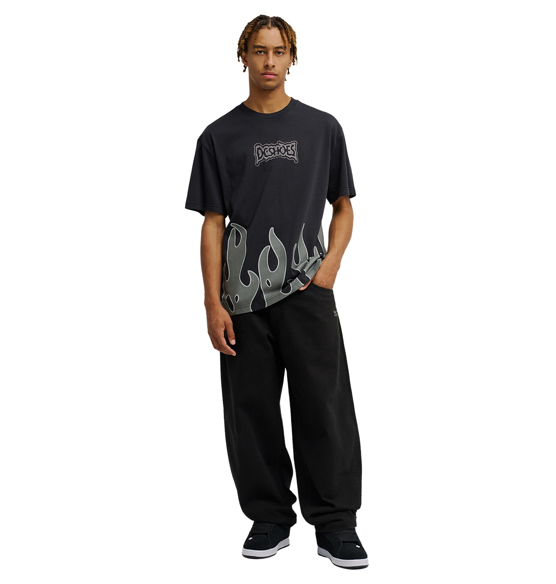 A person wearing the Men's DC Burning Diamonds Tee by DC Shoes, a black graphic skate shirt with a flame design along the bottom, and loose black pants stands facing forward against a plain white background.