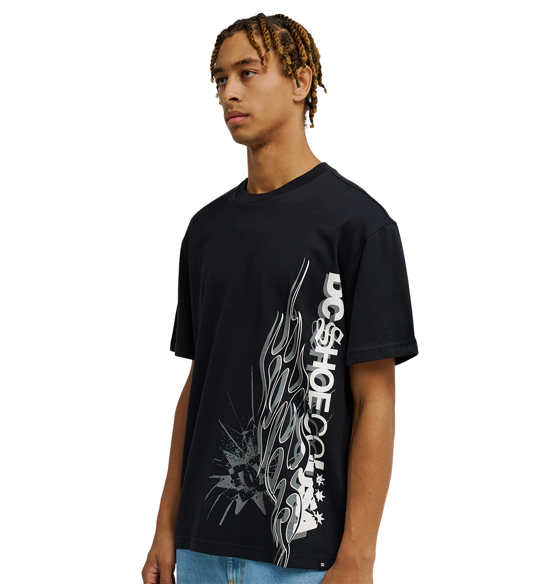 A young man stands against a plain white background wearing the Men's DC Side Flame Tee by DC Shoes, a black t-shirt featuring bold white flame graphics and text on the front—an ideal choice for skate sessions.