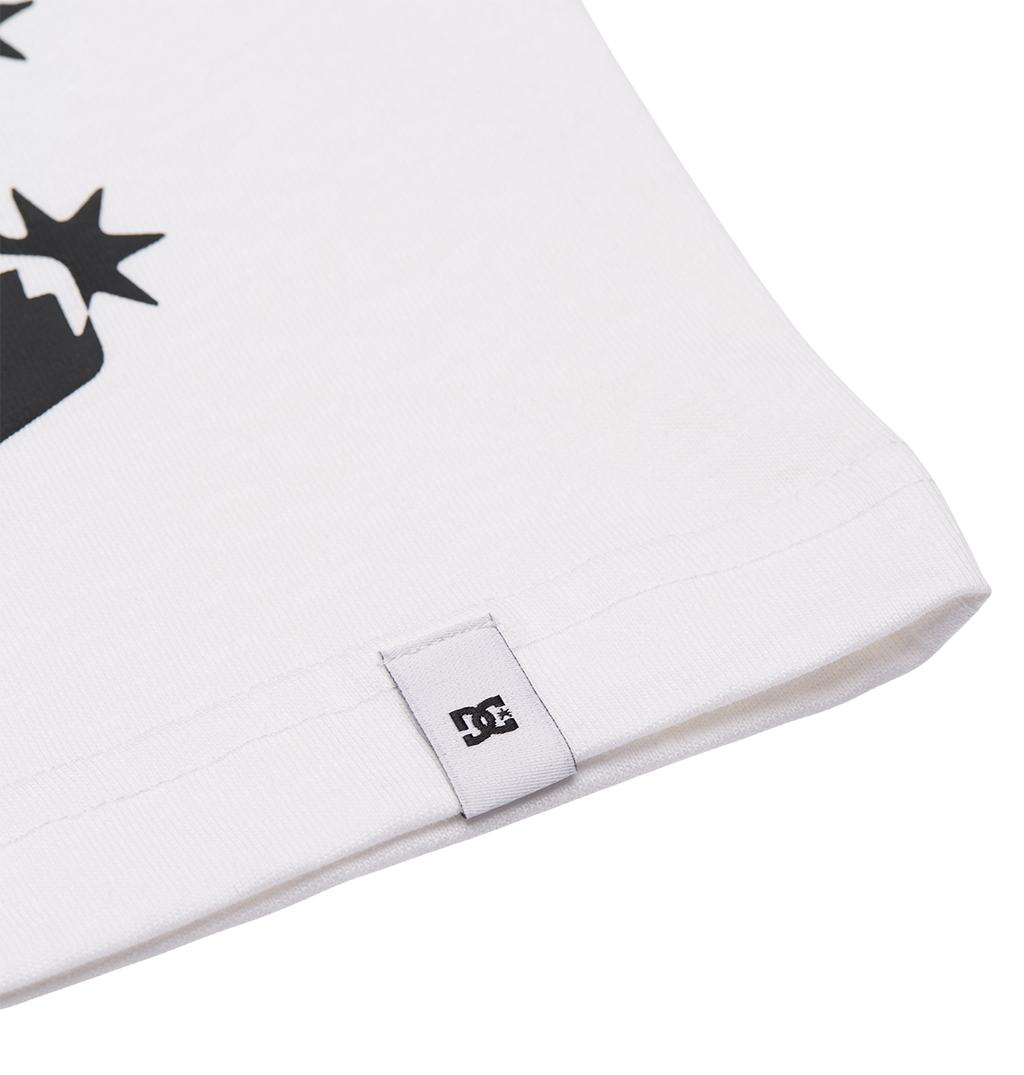 Close-up of the hem on the Men's DC Side Flame Tee by DC Shoes, featuring a small white tag with the black DC Shoes logo. The relaxed fit shirt shows part of its black graphic design against a plain white background.