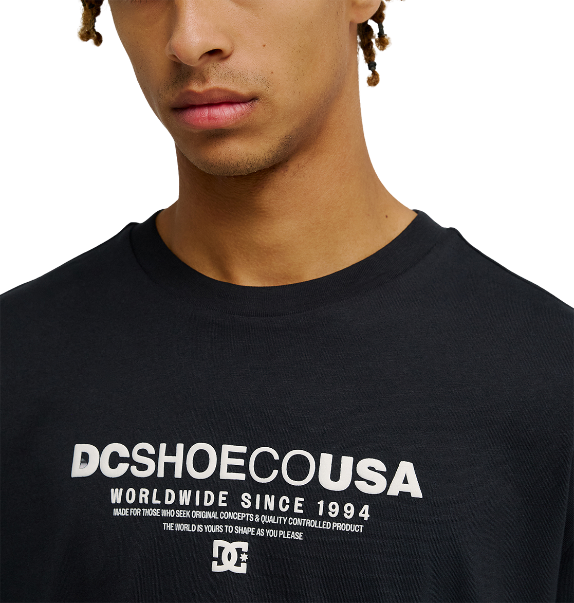 A person wearing the Men's DC Heritage Font Tee by DC Shoes, featuring the bold "DCSHOECOUSA Worldwide Since 1994" graphic across the chest. The photo shows only the lower half of the face and upper torso, emphasizing the relaxed fit of this black skate t-shirt.