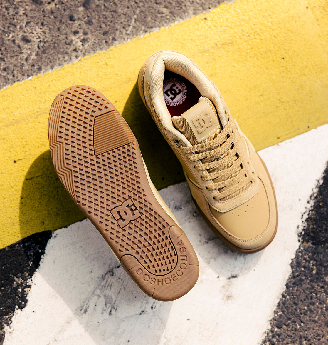 A pair of DC Shoes Men's Fractal S Shoes in tan, with one shoe upright and the other displaying the textured sole, are set on a street marked by yellow and white painted lines—an ideal scene to highlight their street-ready style and performance-driven comfort.