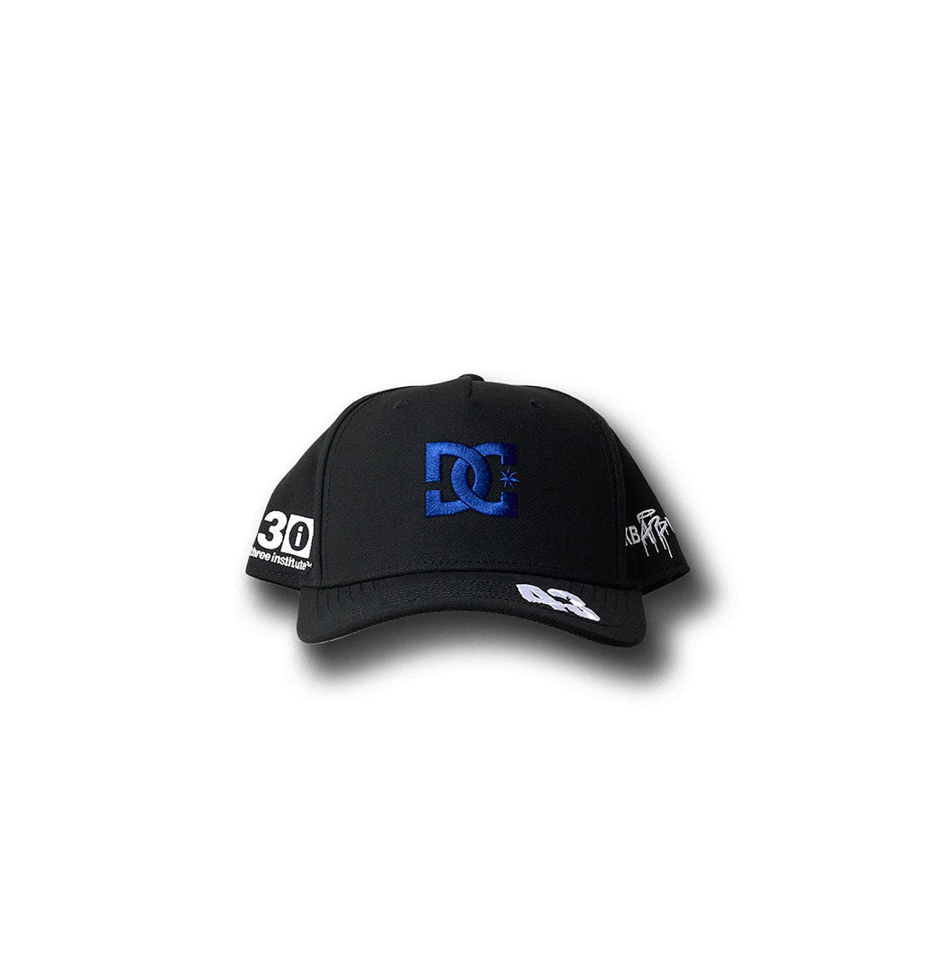 The KB 43 Snapback by DC Shoes is a black baseball cap from the Ken’s Rally Teamworks Collection, showcasing a bold blue logo embroidered on the front and striking white BLOCK print graphic details on the visor and sides, presented against a white background.